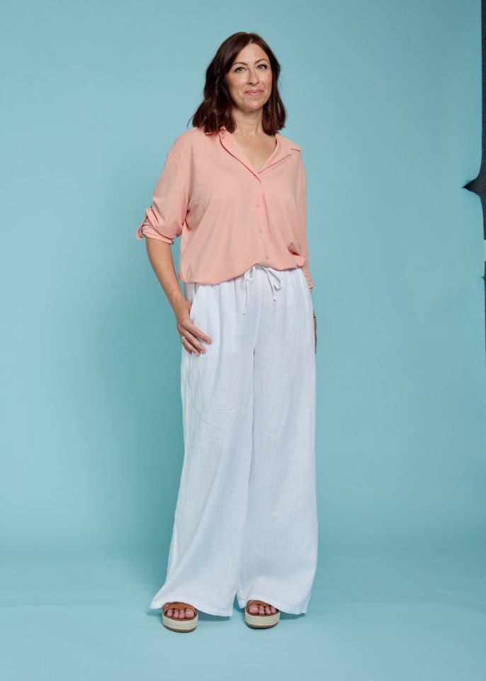 Woman wearing a peach shirt and white linen trousers.