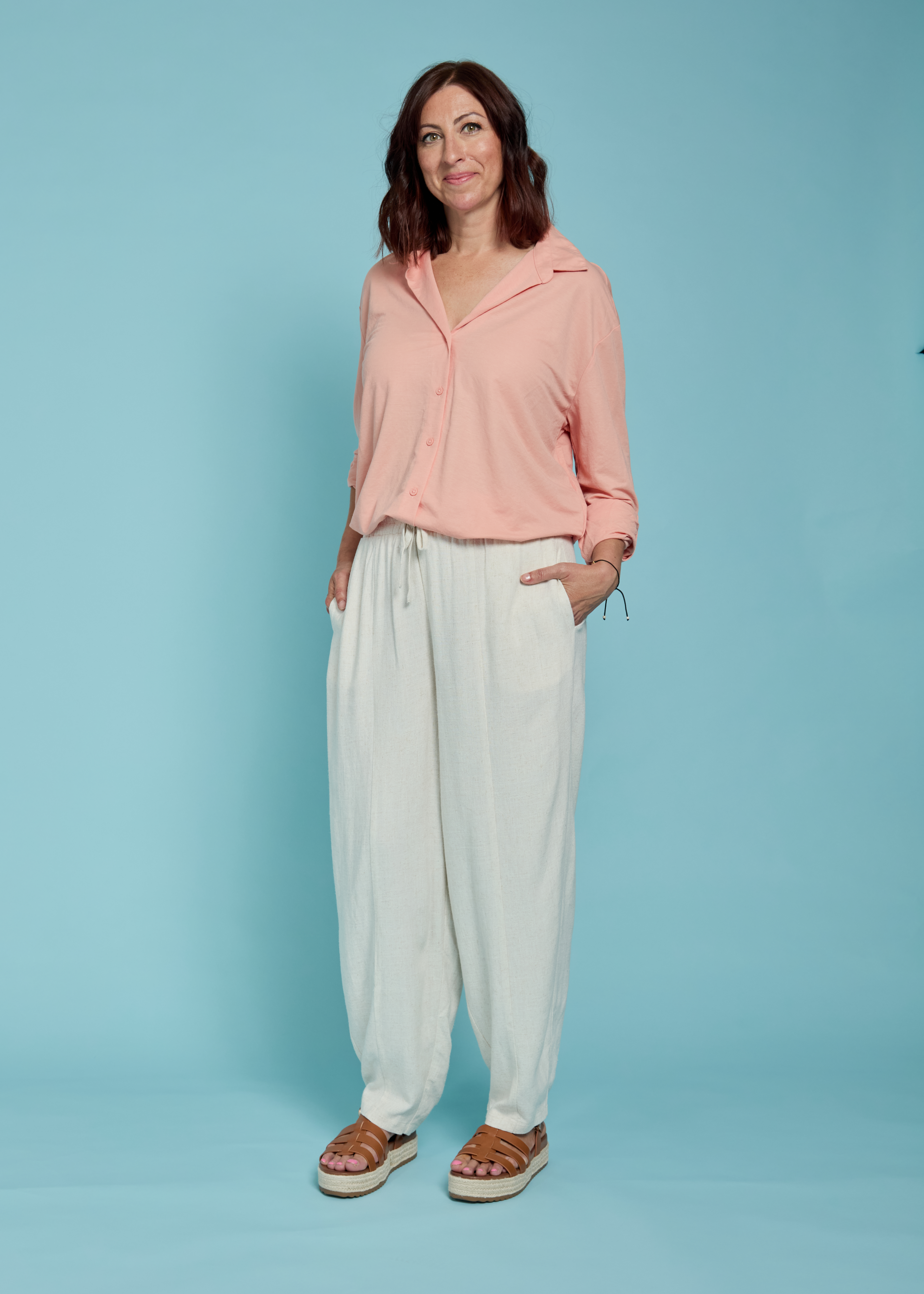 Woman wearing linen trousers and a peach shirt.