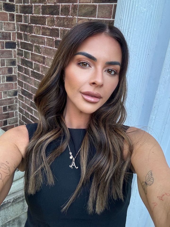 Woman with long brown hair and tattoos wearing a black top and necklace.