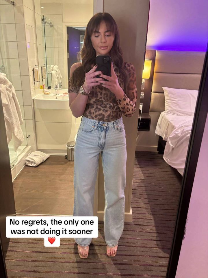 Woman in leopard-print top and light wash jeans taking a selfie in a hotel room.