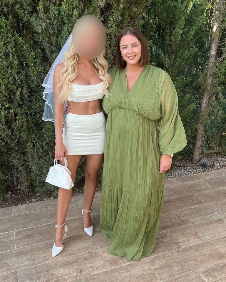 Two women posing for a photo; one in a white bridal-style outfit, the other in a green maxi dress.