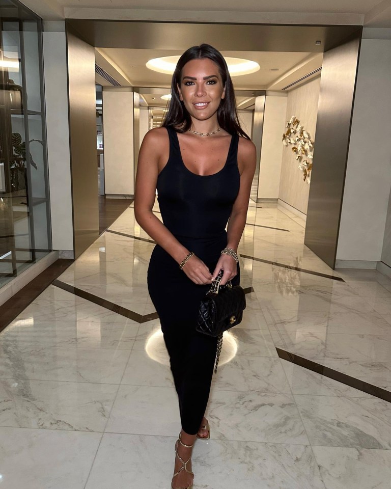 Woman in black dress and gold heels in a hallway.
