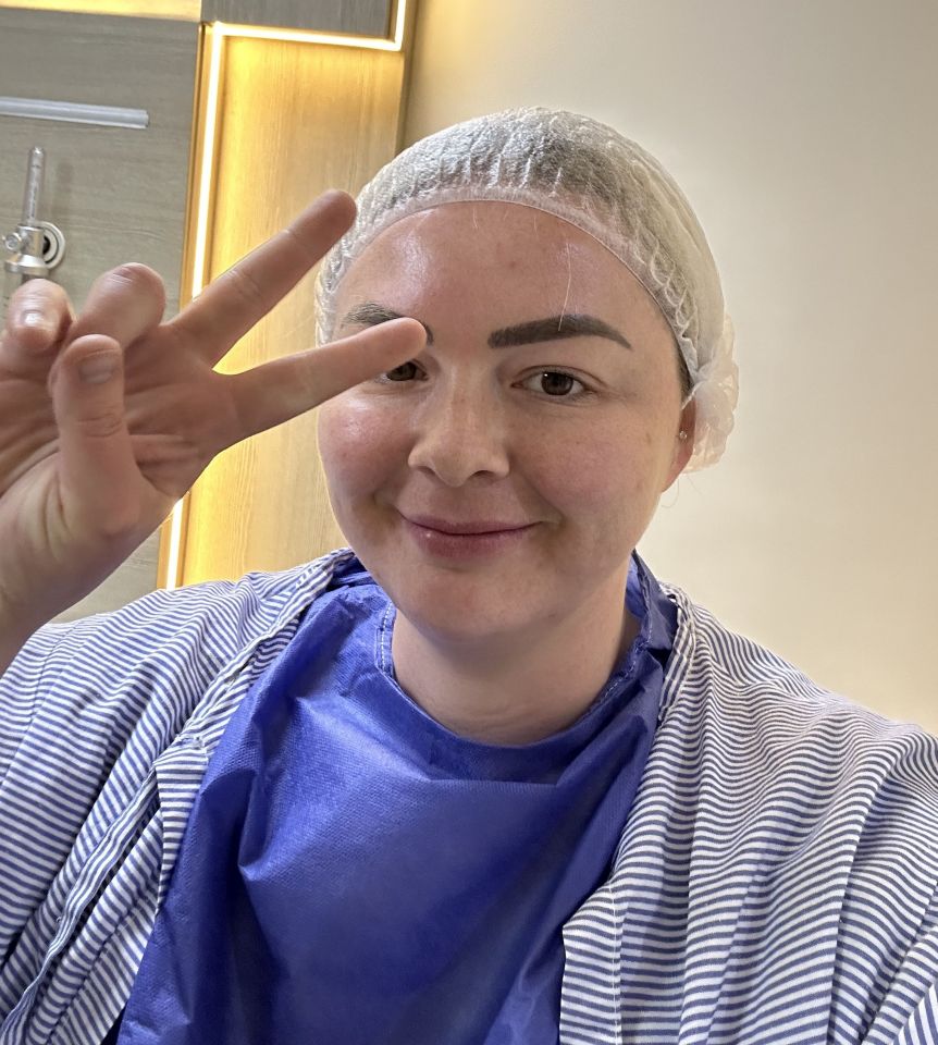 Woman in a surgical cap and gown giving a peace sign.