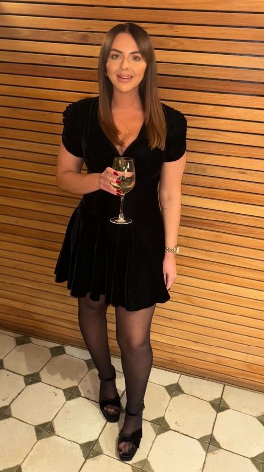Woman in black velvet dress holding a glass of wine.