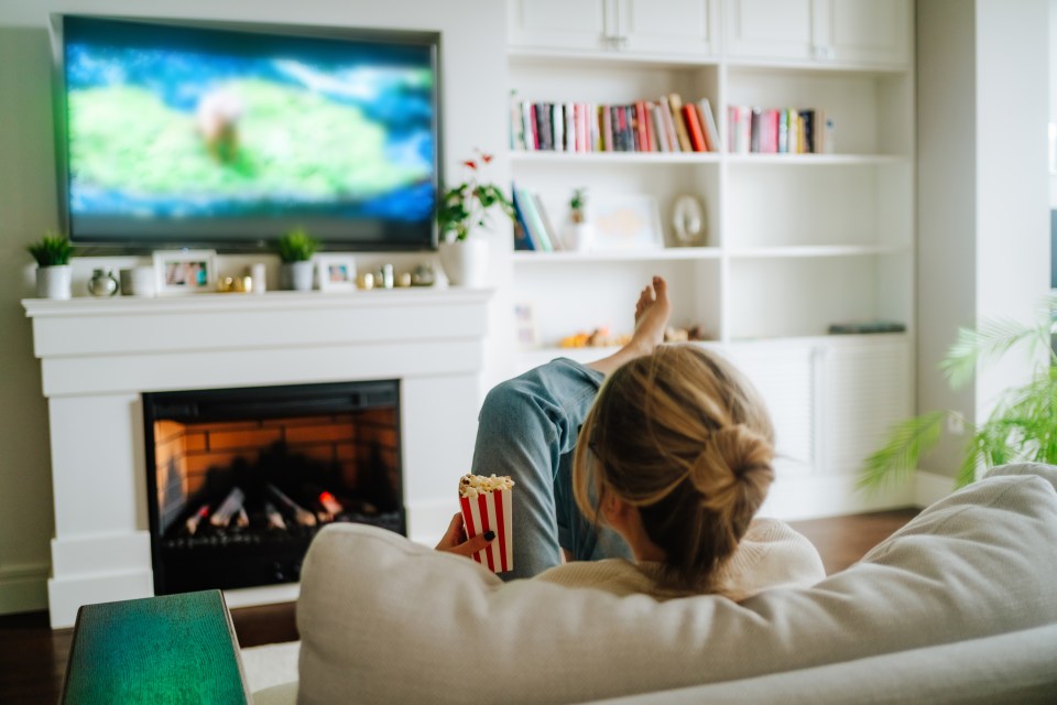 Woman relaxing on a couch, watching TV and eating popcorn.