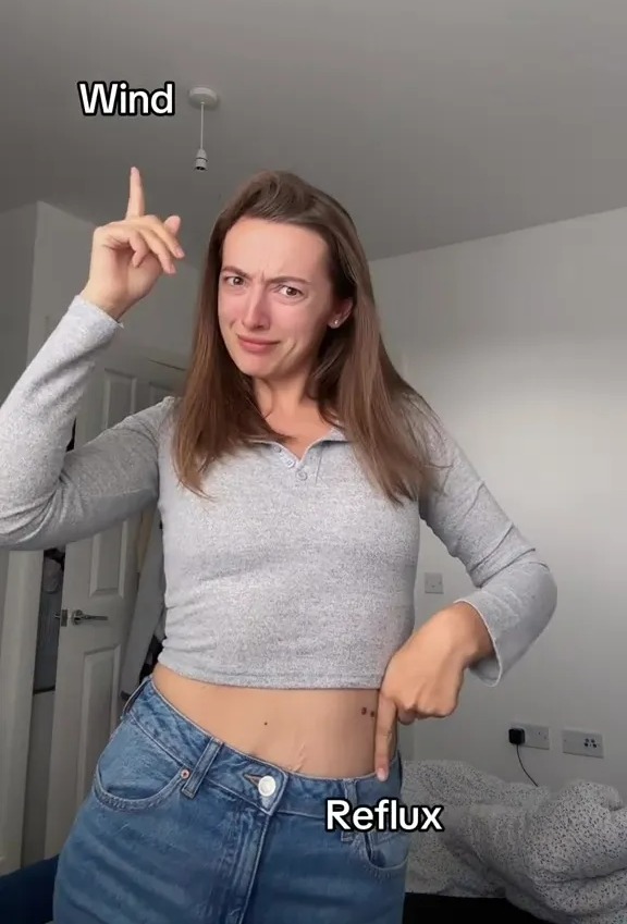 Woman pointing to her stomach and ceiling, illustrating wind and reflux.