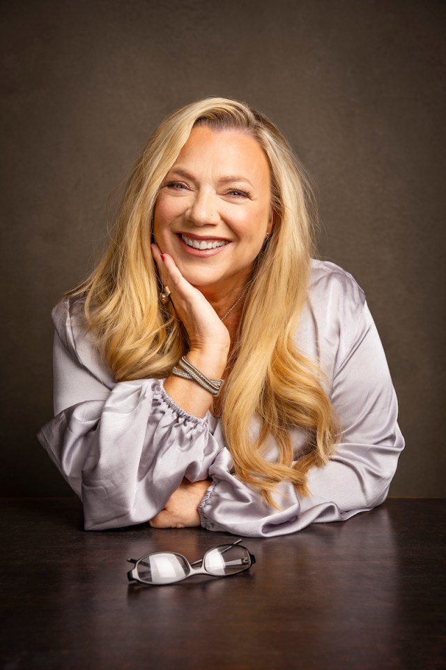 Portrait of a smiling woman with long blonde hair, wearing a lavender blouse.