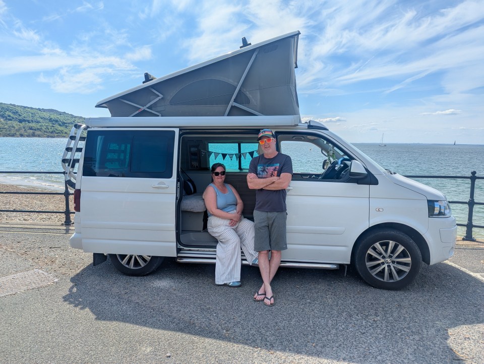 Couple standing by their campervan near the ocean.