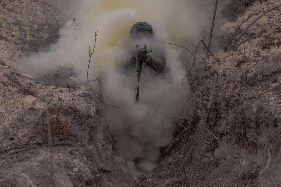 Azov Brigade soldier in a trench during military training amidst smoke.