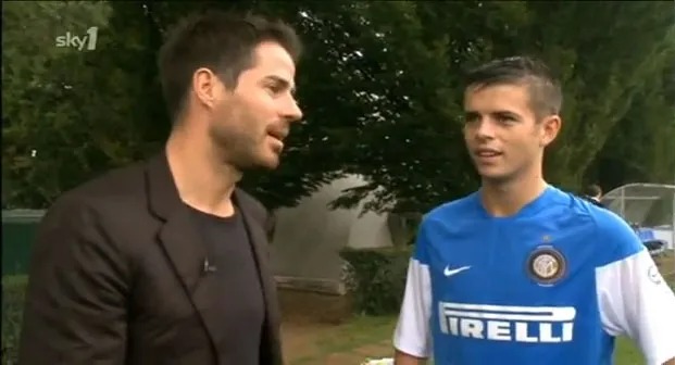 Two men talking, one in a suit, the other in a soccer jersey.