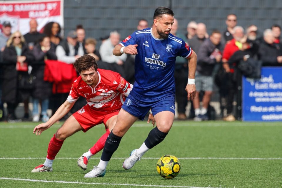 Soccer player in blue jersey dribbling the ball past a player in red.