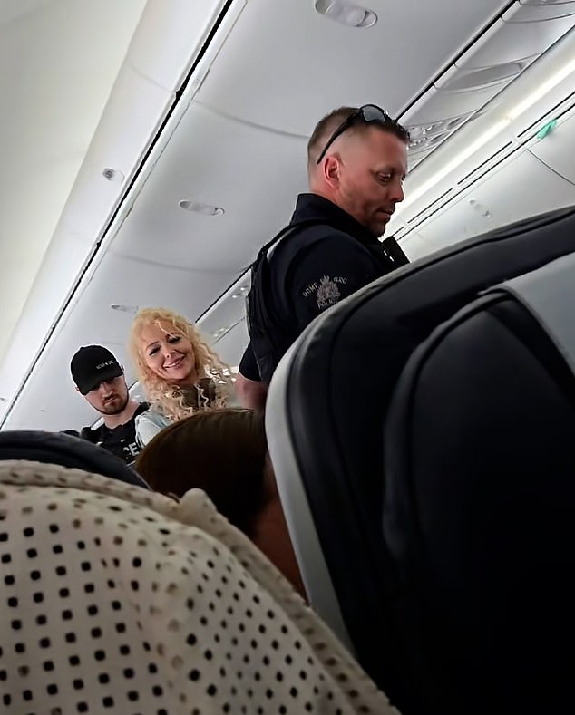 The daughter can be seen smiling and telling the other passengers 'bye' as she is led off the aircraft in handcuffs