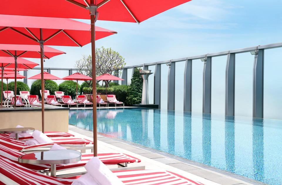 Rooftop pool with red and white striped lounge chairs and red umbrellas.