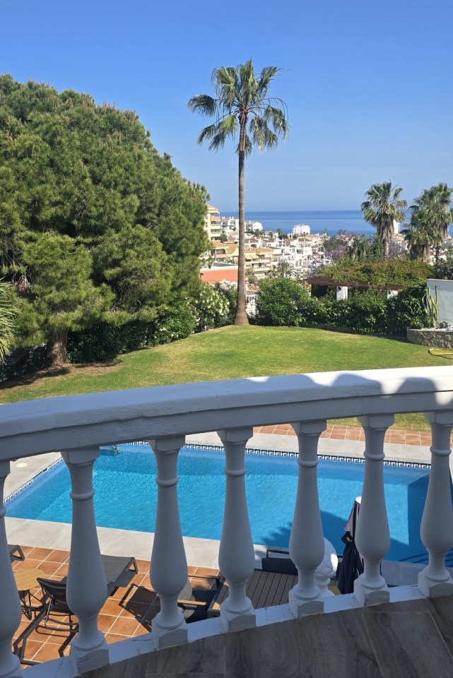 View of a swimming pool and ocean from a balcony.