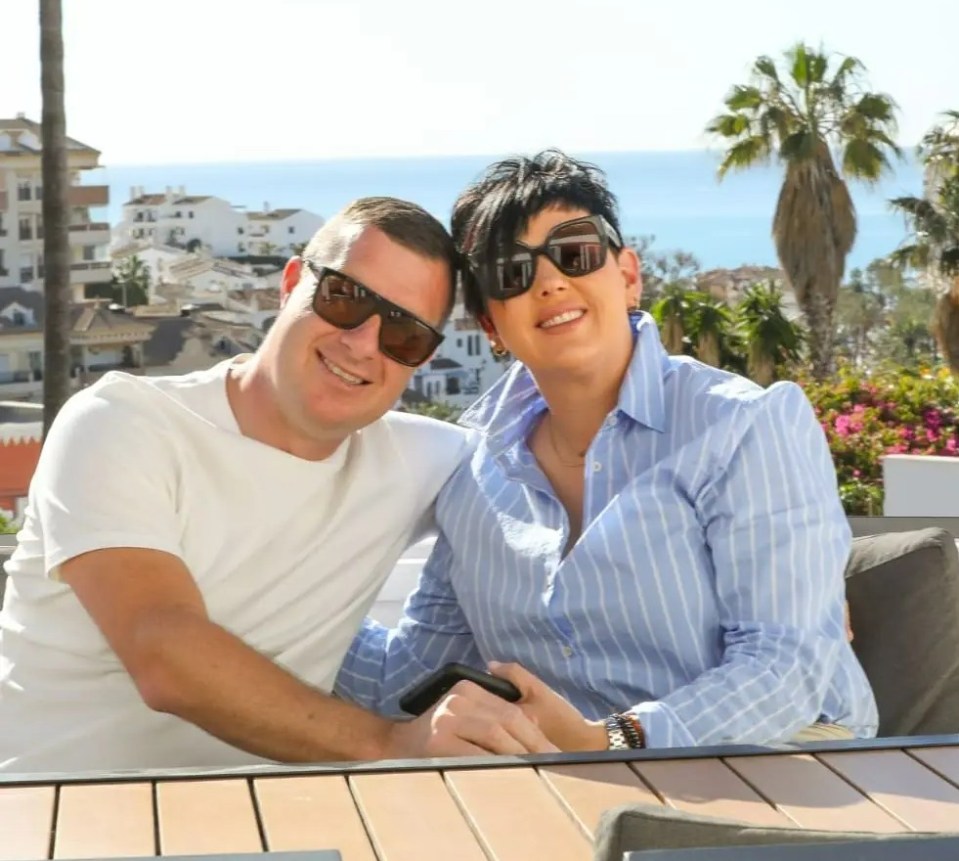 Couple smiling outdoors at a table.