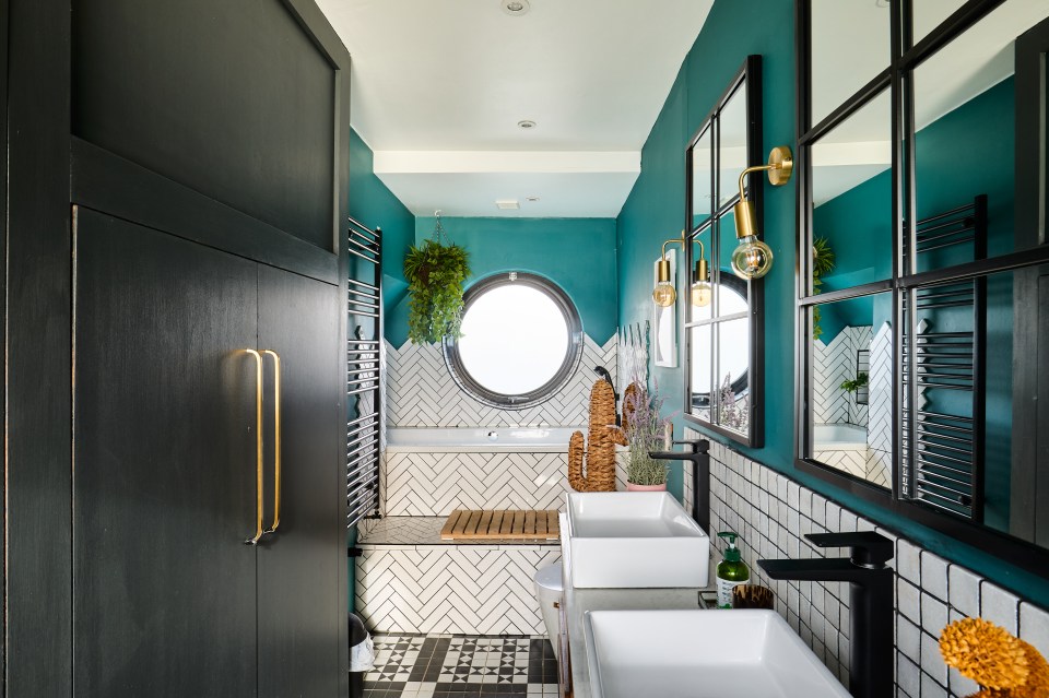 Bathroom interior of a houseboat with teal walls, herringbone tile, and a round window.