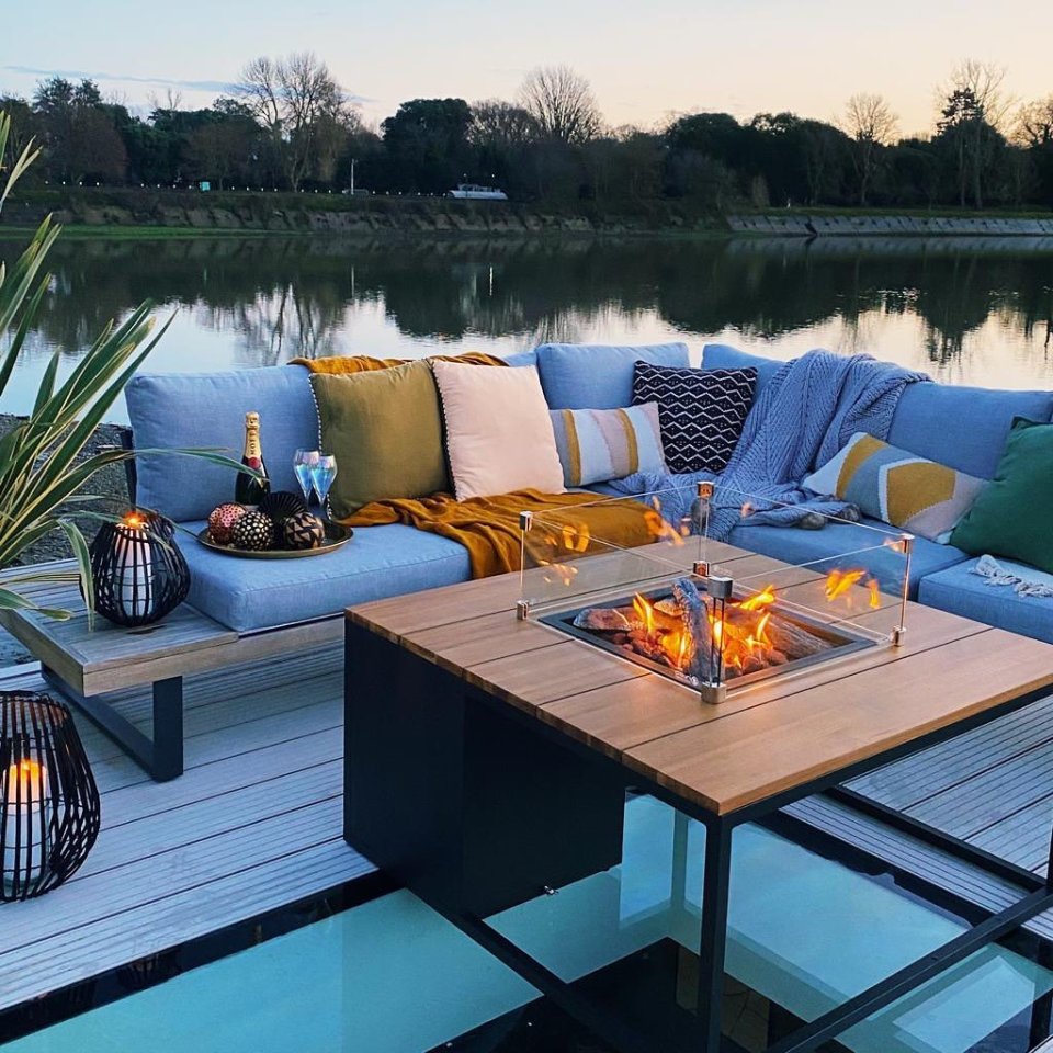 Houseboat patio with fire pit and sectional sofa overlooking a river.