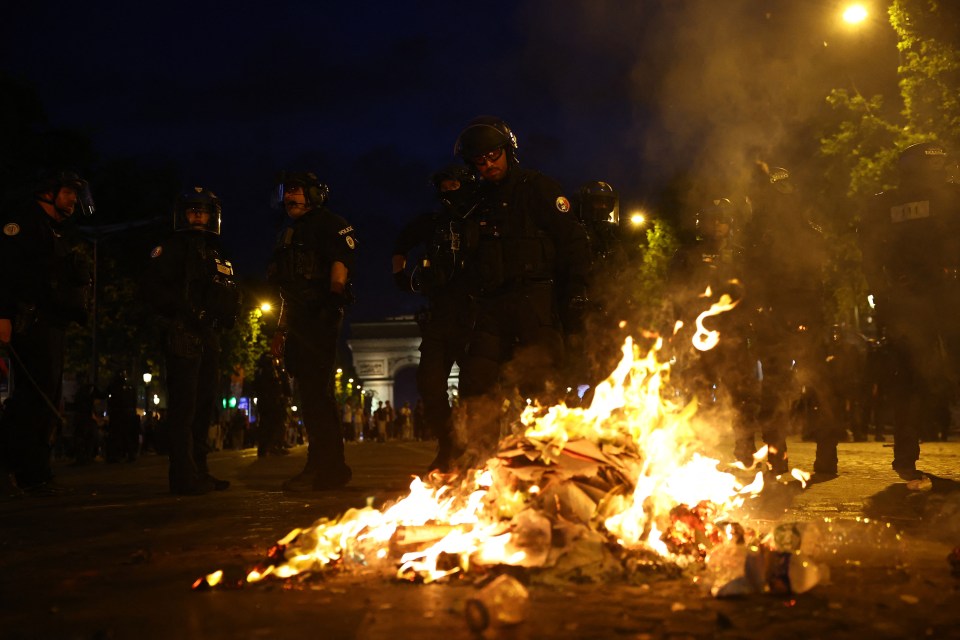 Police officers watching a bonfire during a riot.