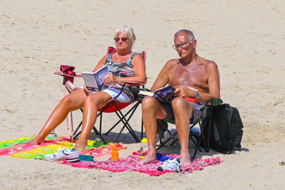 Couple relaxing on a beach, reading books.