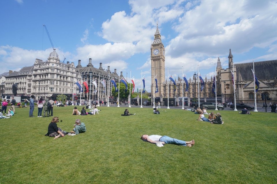 People relaxing on the grass in front of the Houses of Parliament and Big Ben.