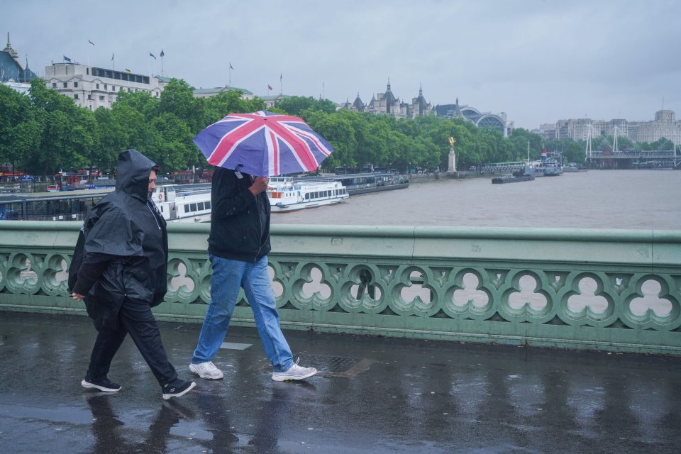 Two pedestrians walking on Westminster Bridge in London, one using a Union Jack umbrella.