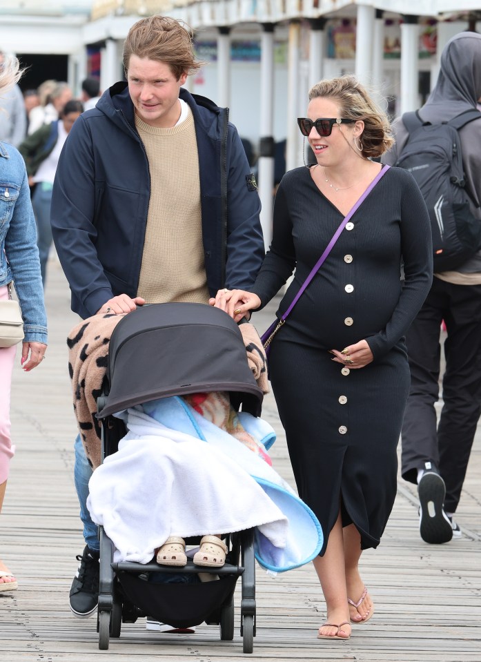 Pregnant Kelsey Parker and her boyfriend stroll along a pier with their child in a stroller.