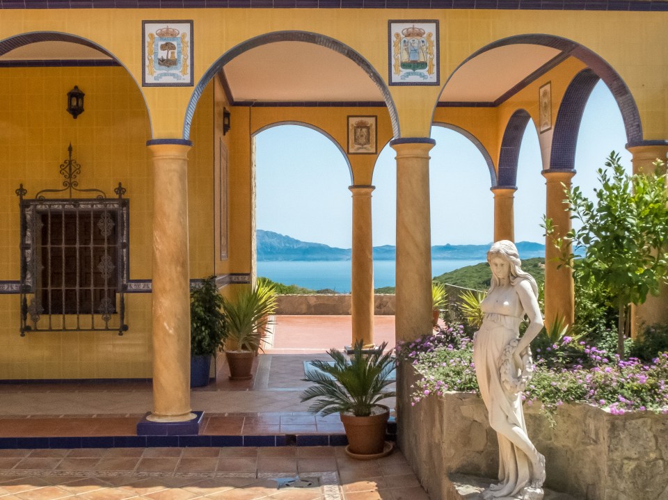 Villa exterior with arched colonnade, statue, and sea view.