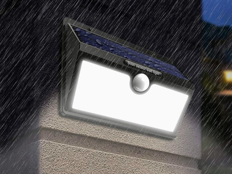Solar-powered motion sensor security light mounted on a wall in the rain.