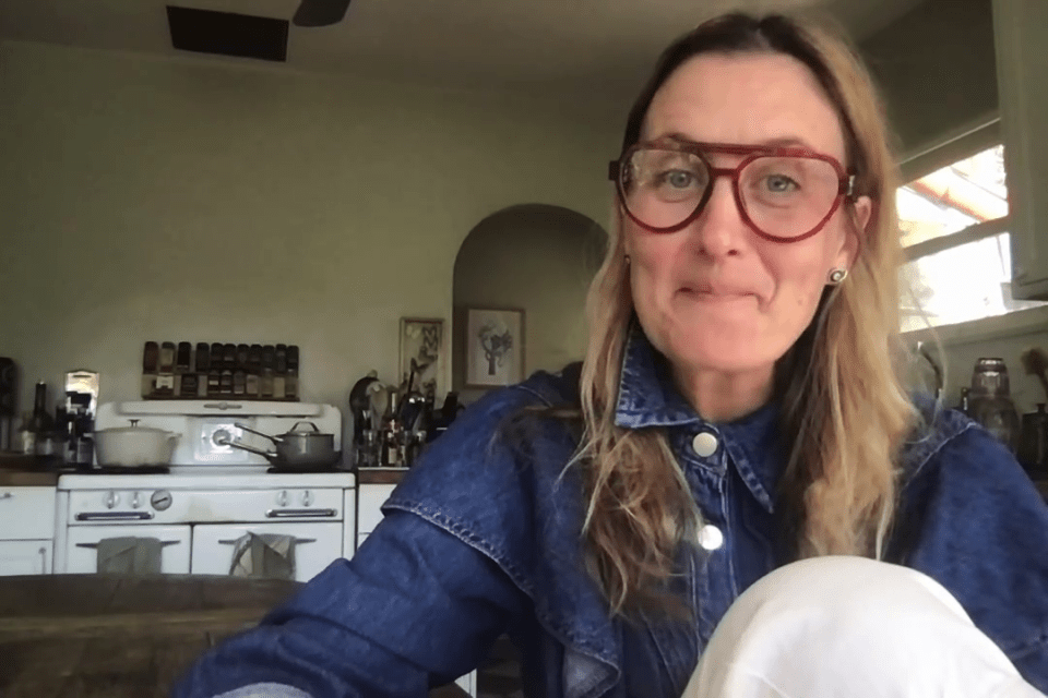 Tempany Deckert in a denim jacket, speaking to camera in her kitchen.