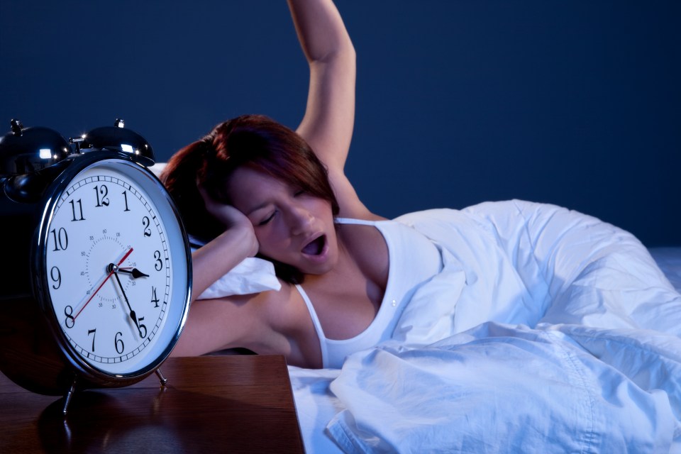 Woman waking up in bed next to an alarm clock.