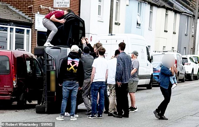 The photo was taken by a by-stander and shows the men on top of the black car after the crash on a residential road in Kent