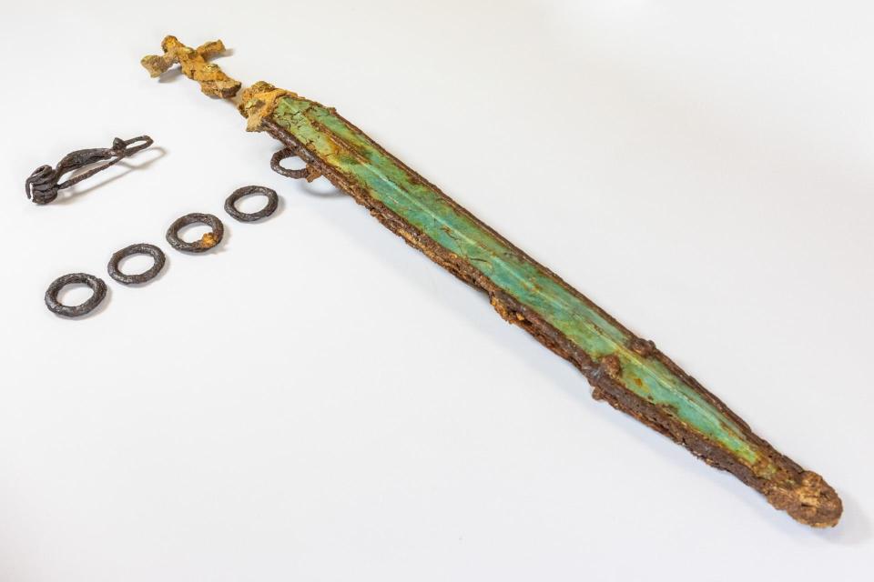 Rusty sword, fibula, and belt rings from a burial.