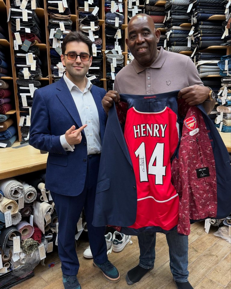 Man holding up a suit jacket with a Thierry Henry Arsenal jersey inside.