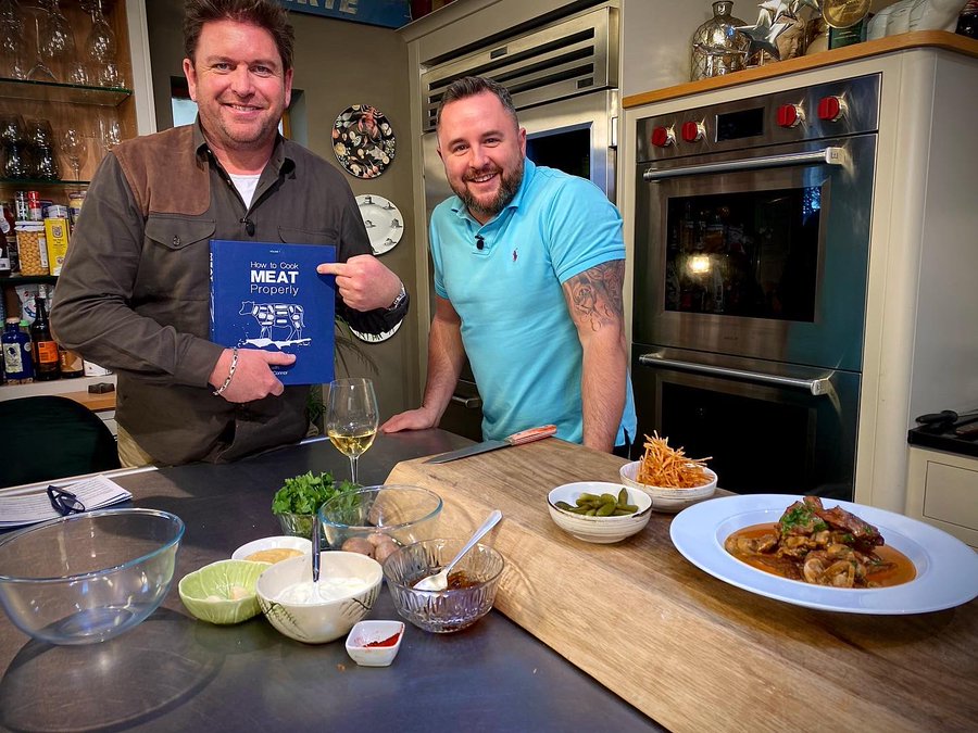 Two chefs in a kitchen, one holding a cookbook titled "How to Cook Meat Properly".