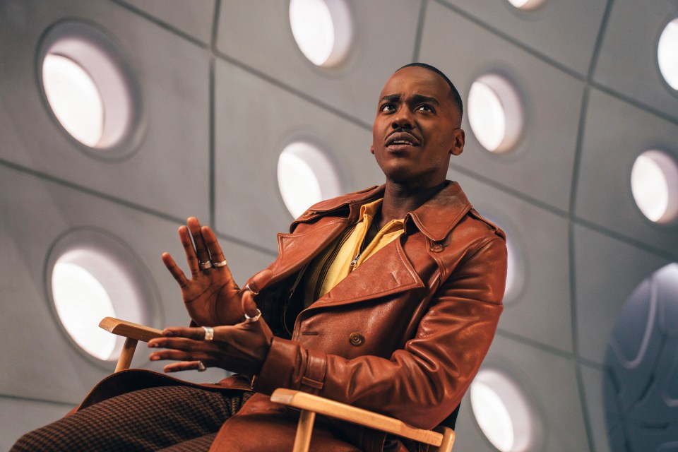 Ncuti Gatwa as the Doctor in a brown leather jacket, looking upward.