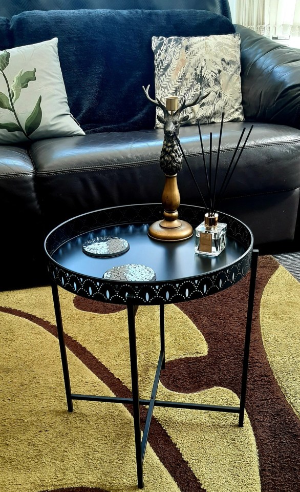 Black side table with coasters, candle holder, and reed diffuser.