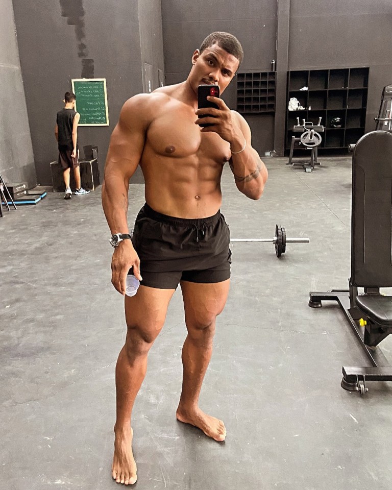 A muscular man takes a selfie in a gym.