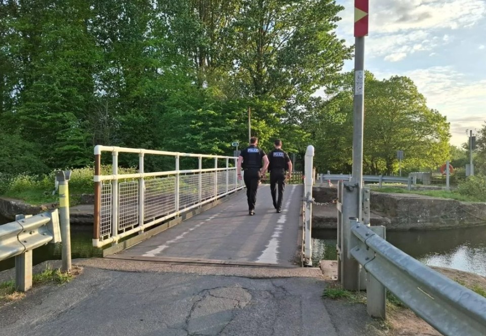 Two police officers walking on a bridge over a canal.