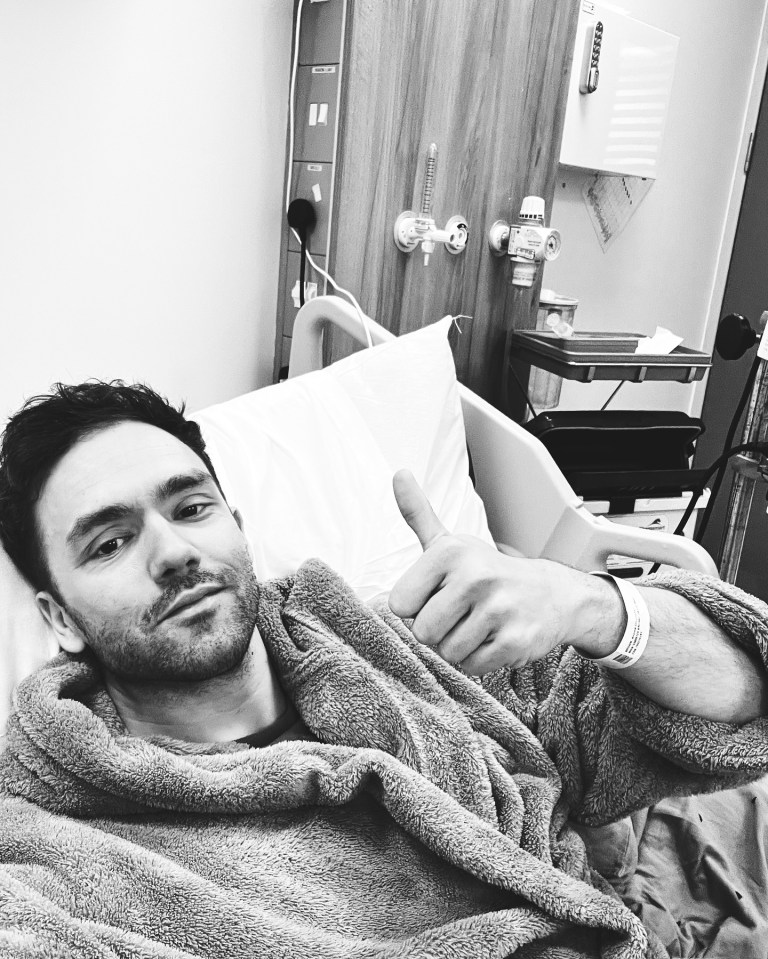 Black and white photo of a man in a hospital bed giving a thumbs up.