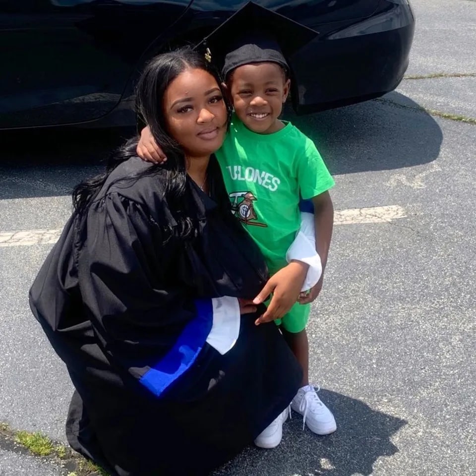 A graduating woman in a cap and gown embraces her young child.