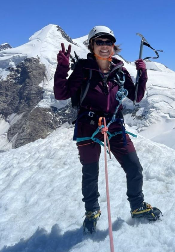 A woman mountain climber poses on a snowy peak, giving a peace sign.