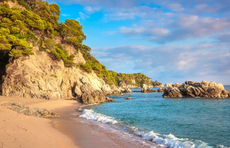 Sandy beach with rocky cliffs and clear blue water.