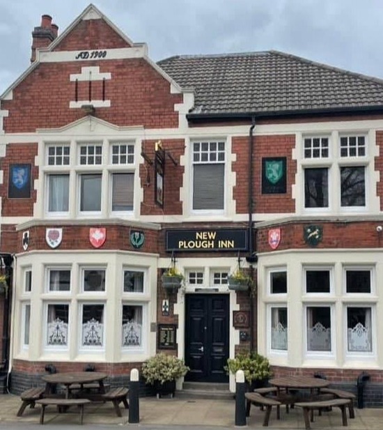The New Plough Inn, a brick building with multiple windows and hanging baskets.