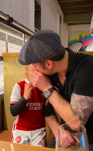 A man kisses a child wearing an Arsenal soccer jersey.