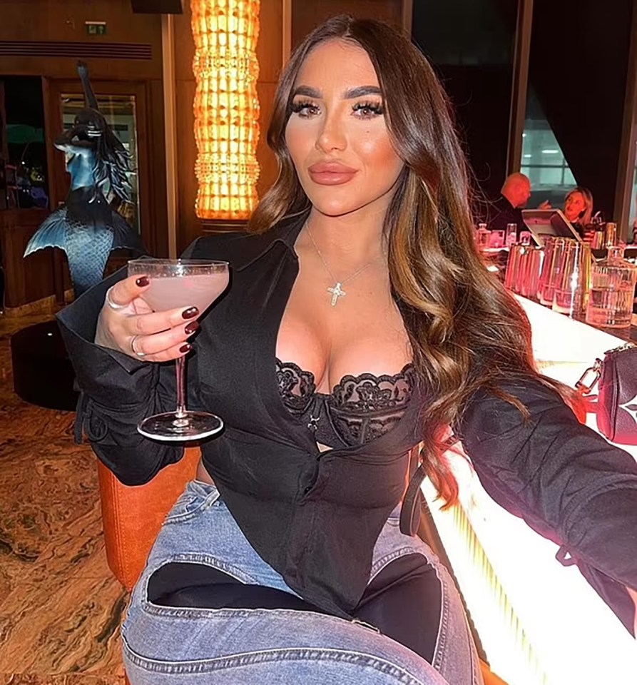 Woman in black shirt and jeans holding a cocktail at a bar.