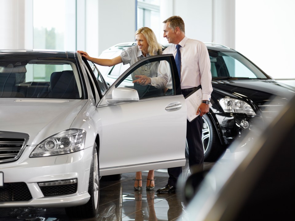 A salesperson shows a couple a new car at a dealership.