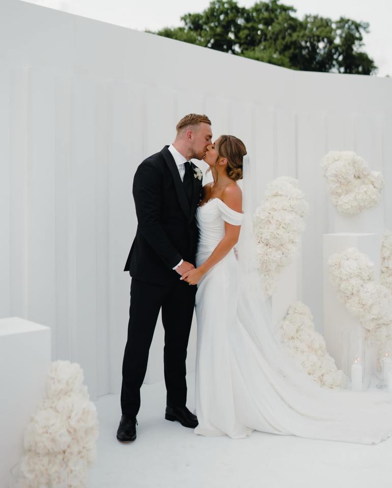 Bride and groom kissing in front of a white floral backdrop.