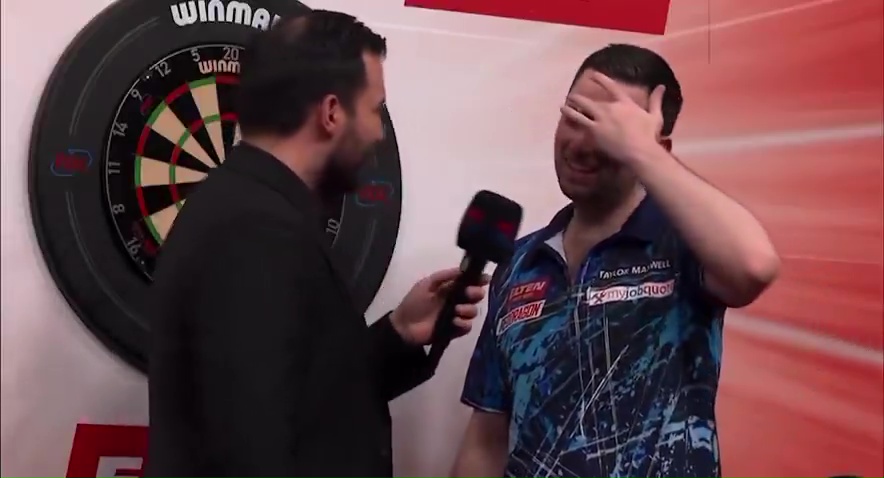 A darts player covers his face while being interviewed.
