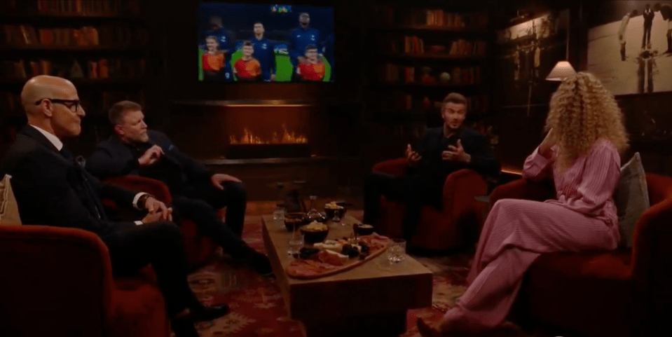 Screenshot of four people sitting in armchairs around a coffee table, watching a soccer game on a television screen.