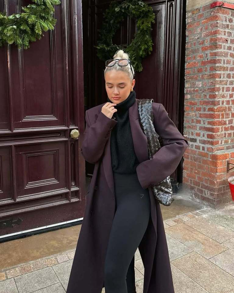 Woman in a long dark purple coat and black leggings.